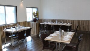 Un restaurante con varias mesas dispuestas para comer, sillas y una planta en maceta.