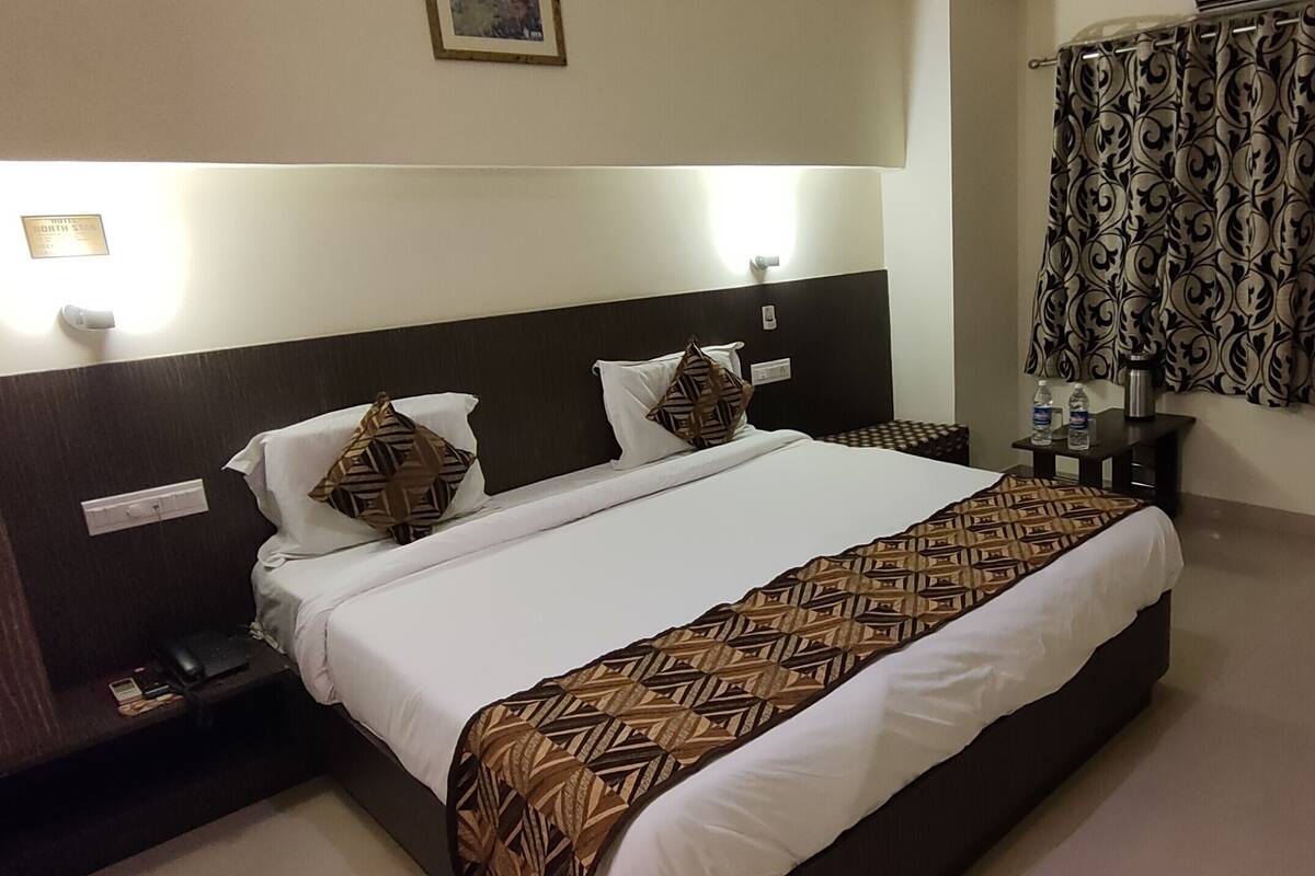 A hotel room with a large bed, bedside tables, a desk, and a patterned curtain.