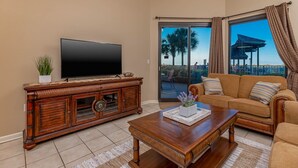 Una sala de estar con televisor de pantalla plana, mueble de madera para entretenimiento y un sofá con vista al exterior.