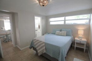 A bedroom with a bed, bedside tables, a lamp, a window, and a door leading to a bathroom.