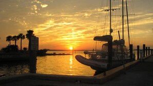 A sunset over a marina with a boat docked, palm trees, and a sign prohibiting swimming, fishing, and canoeing.
