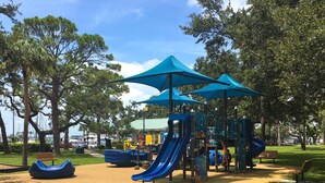 A playground with slides and climbing structures, surrounded by benches and trees.