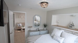 A bedroom with a bed, bedside table, dresser, and a large mirror.