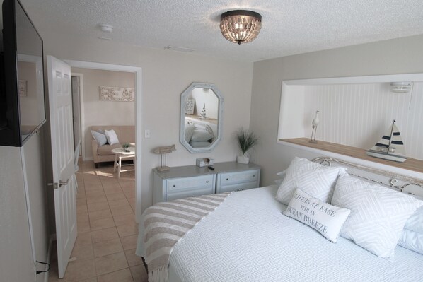A bedroom with a bed, bedside table, dresser, and a large mirror.