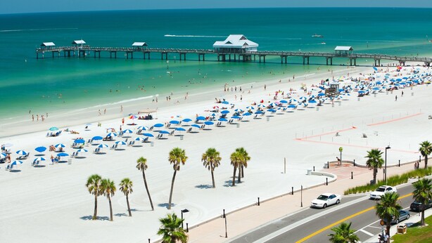 A beach with a pier, umbrellas, and palm trees.