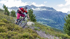 Um ciclista de montanha numa trilha, com montanhas ao fundo.