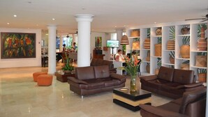 Un vestíbulo amplio con sofás de cuero, una mesa de centro y un cuadro grande en la pared. Hay plantas en macetas y estanterías con objetos decorativos.