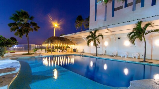 Una piscina con techo de paja, palmeras y sillas de descanso.