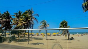 Una playa con palmeras, sombrillas amarillas y un cielo azul despejado.