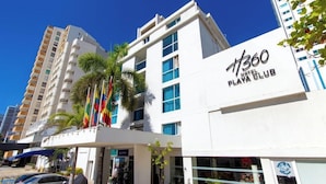 Un hotel moderno con fachada blanca, varios balcones y una entrada destacada con puerta de vidrio.