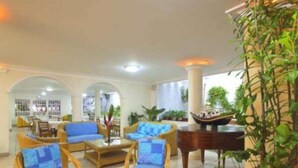 Un hall con muebles de mimbre, una planta grande en maceta y un modelo de barco.