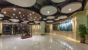 A spacious lobby with a polished floor, circular ceiling lights, a reception desk, and a large abstract art piece. - Linzhen Hotel (Shanghai)