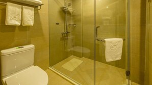 A glass-enclosed shower stall with a toilet and a towel rack in a bathroom with beige tiles. - Linzhen Hotel (Shanghai)