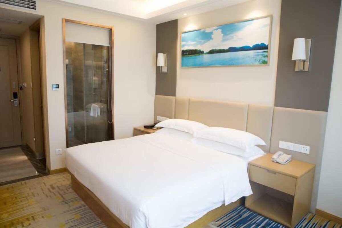 Habitación de hotel con una cama grande, una mesita de noche con un teléfono, un cuadro en la pared y un box de ducha de vidrio.