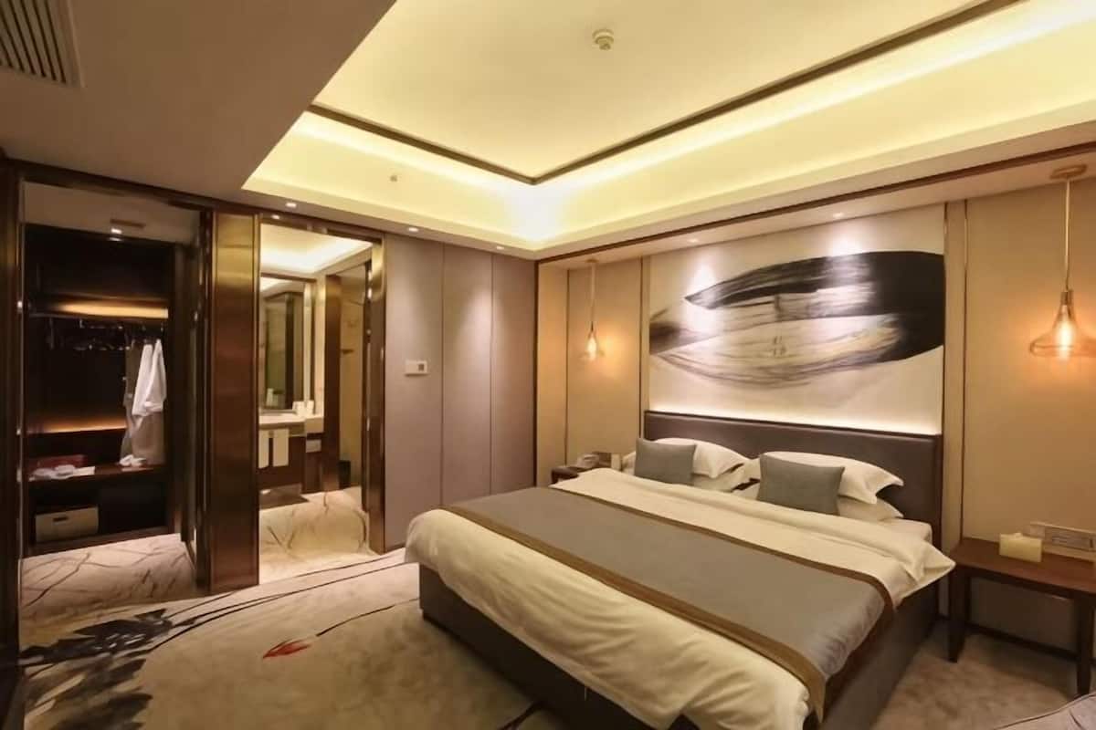 A modern hotel room with a large bed, a walk-in closet, and a large abstract painting on the wall.