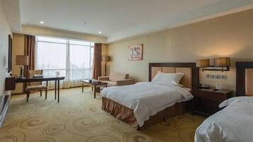 A hotel room with two beds, a desk, a chair, a lamp, and a window.