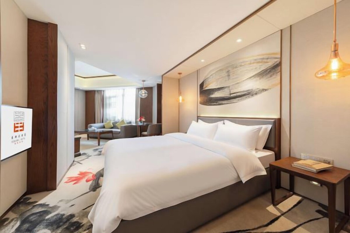 Quarto de hotel moderno com uma cama grande, uma mesinha de cabeceira, uma televisão na parede e um quadro.