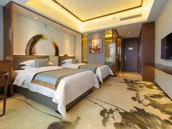 A hotel room with two beds, a large artwork on the wall, and a TV mounted on the wall. - Donghu Grand Hotel (Jieyang)