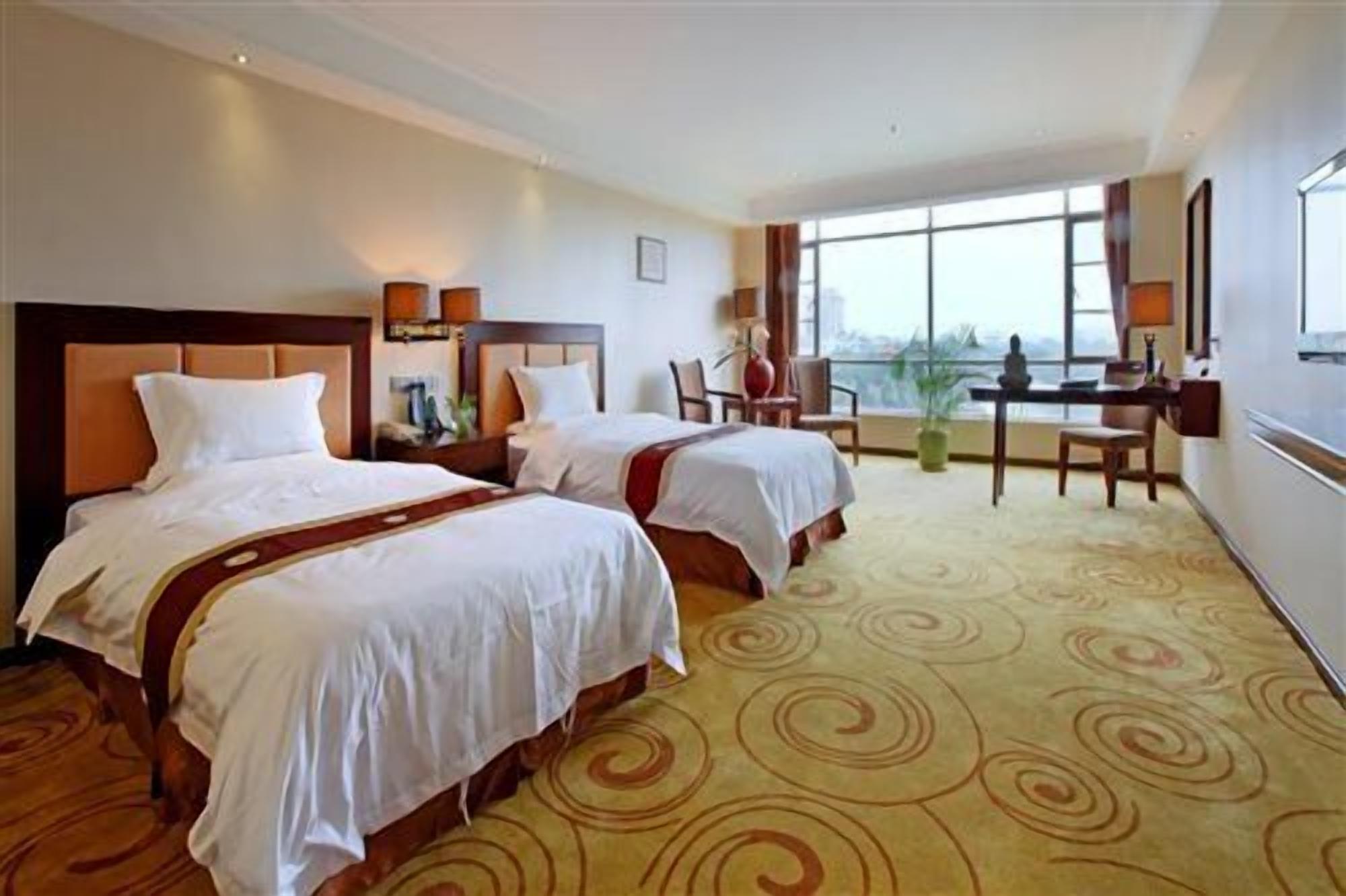 Una habitación de hotel con dos camas, un escritorio, una silla y un ventanal grande.
