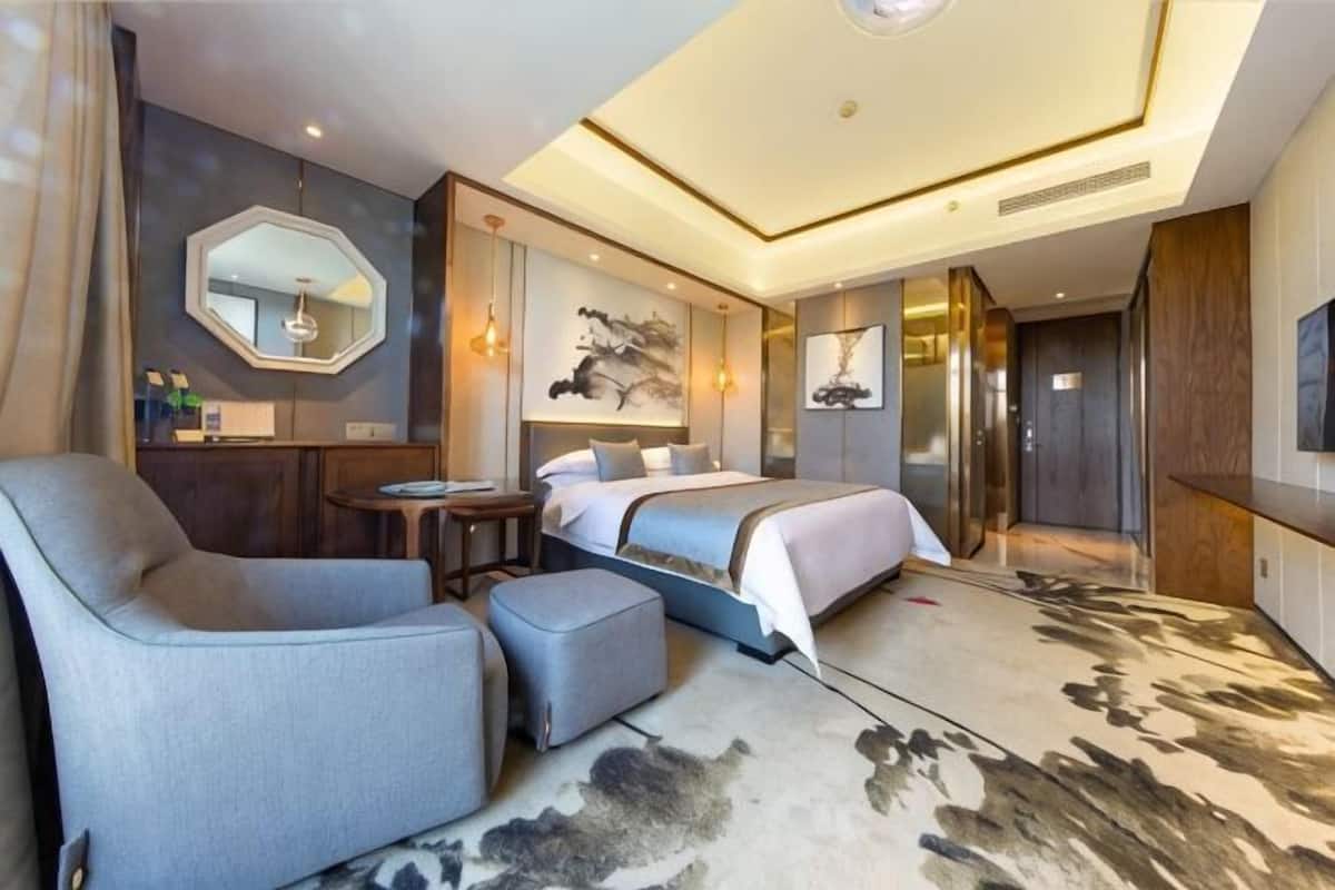 A hotel room with a bed, a desk, a chair, a small table, and a large mirror.