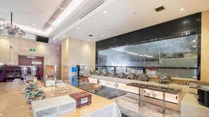 Un vestíbulo moderno de hotel con mostrador de recepción, un amplio ventanal y zona de bufé con varios recipientes de comida.