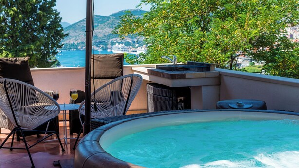 Een zwembad op het dak met uitzicht op zee, een tafel met stoelen en een jacuzzi.
