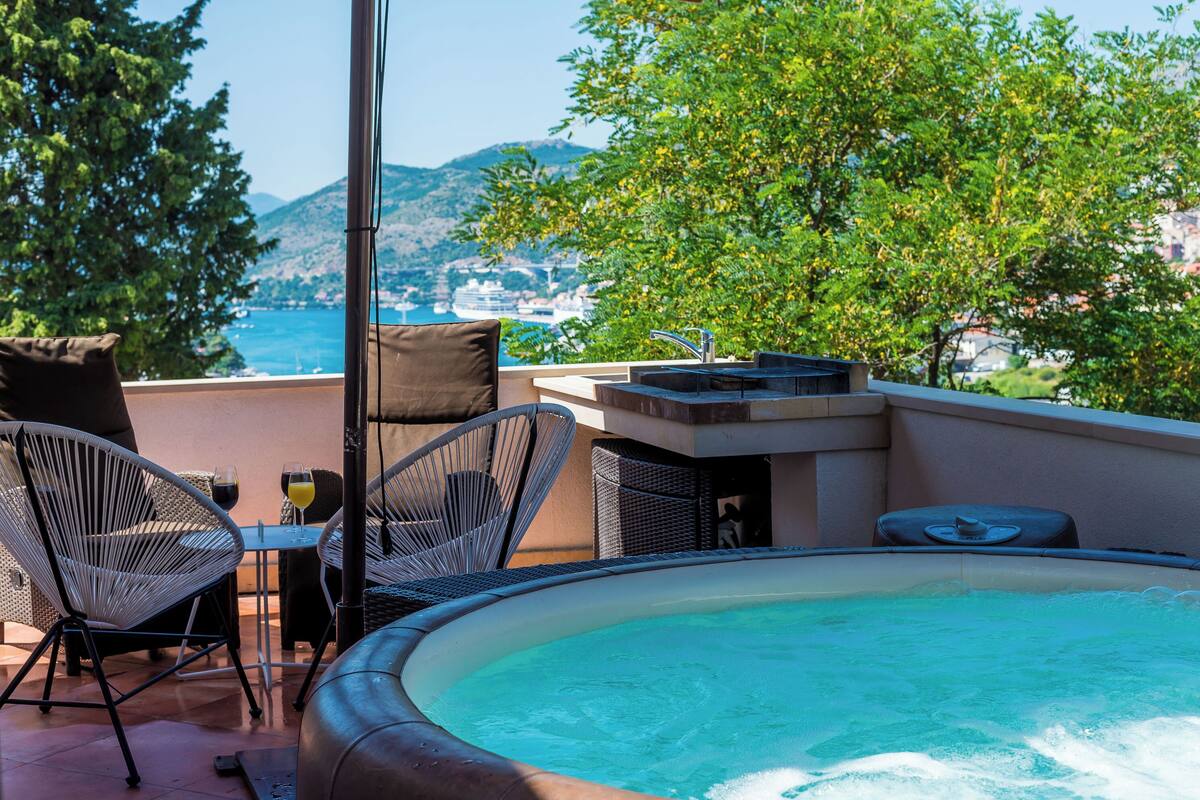 Un área de piscina en la azotea con vista al mar, una mesa con sillas y un jacuzzi.