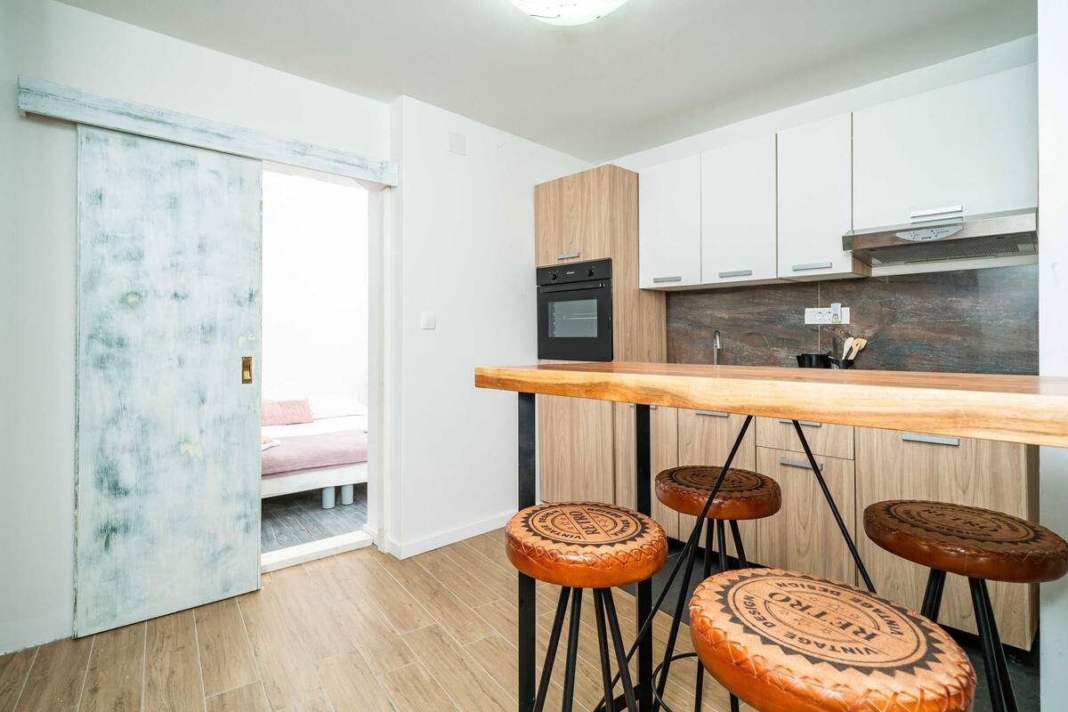 Una cocina moderna con encimera de madera, estufa negra y tres taburetes con asientos redondos.