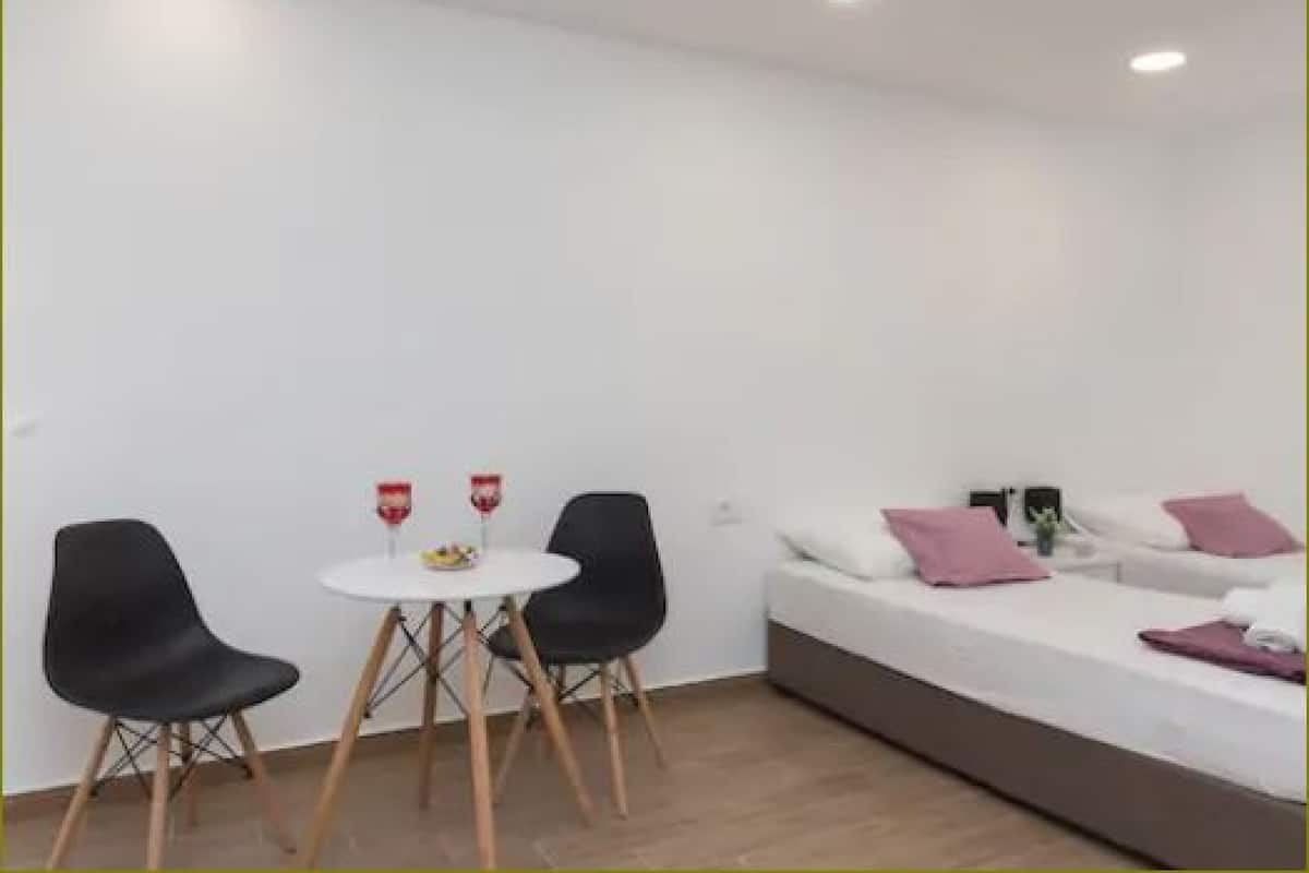Una habitación moderna con una cama blanca, sillas negras y una mesita redonda con dos vasos.