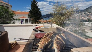 Een dakgrill met vis die gebakken wordt, met uitzicht op een stadslandschap met gebouwen en een berg op de achtergrond.