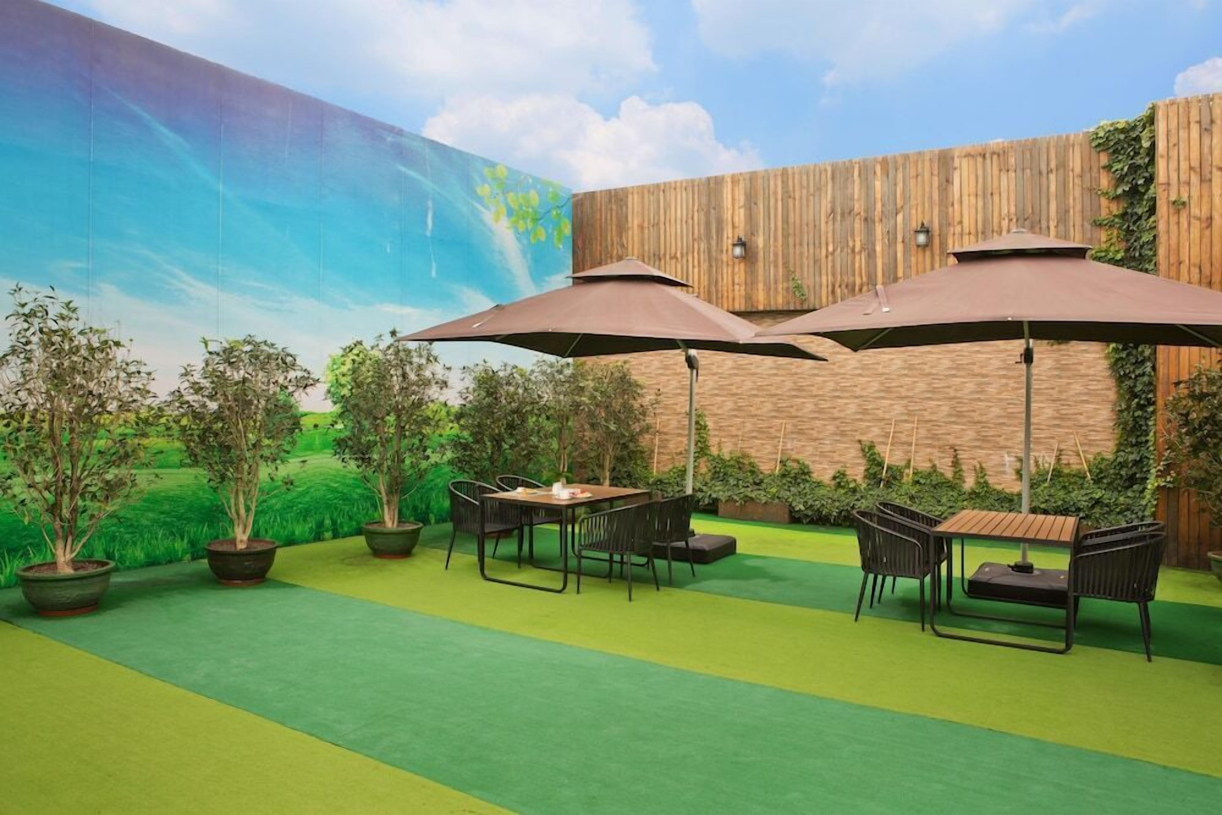 An outdoor patio with a wooden fence, green artificial turf, potted plants, and a mural of a landscape.