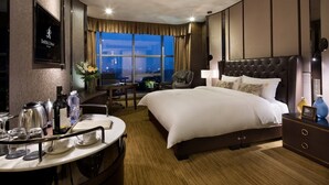 Habitación de hotel con una cama grande, un escritorio con silla, televisor montado en la pared y ventana con vista a la ciudad de noche.
