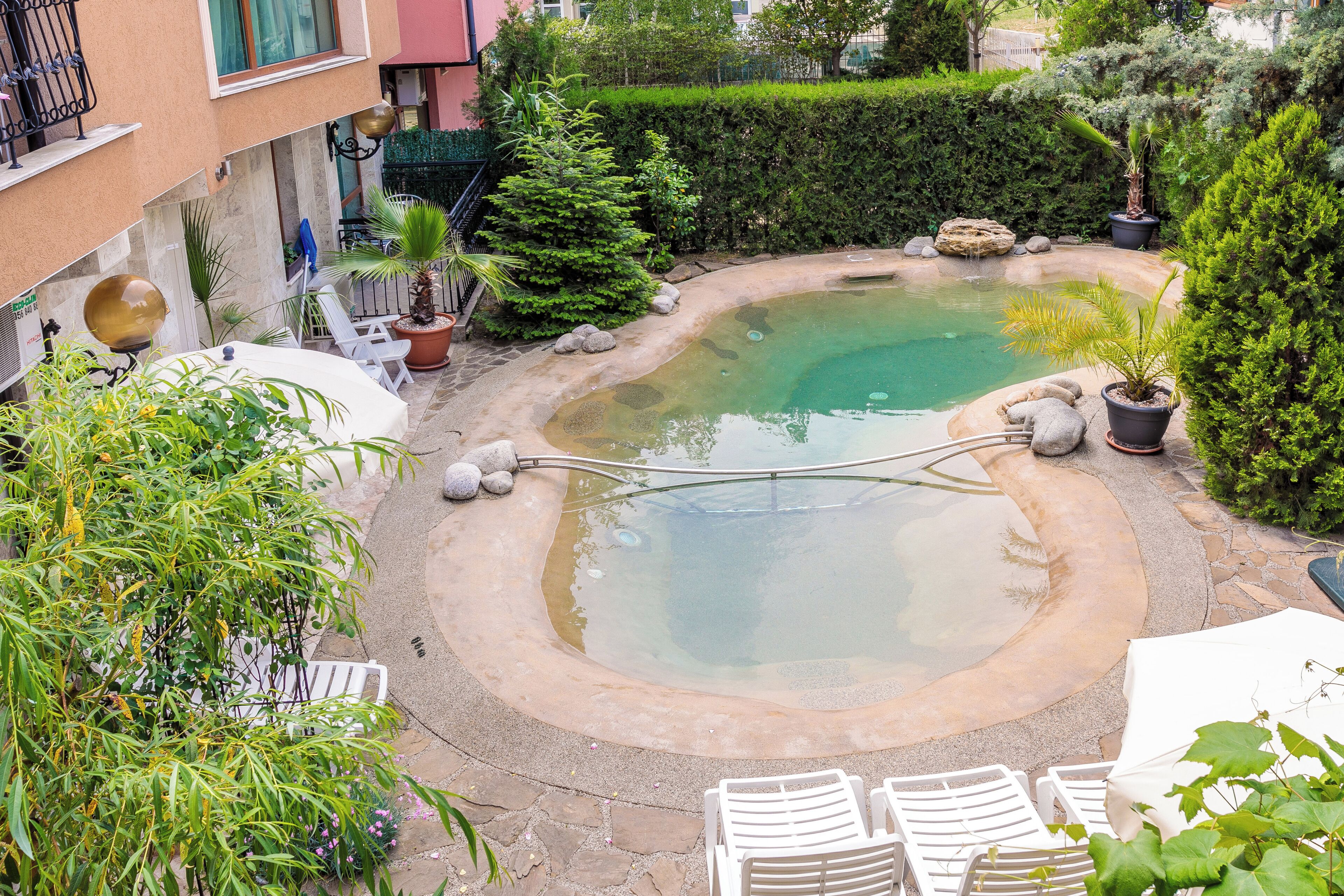 A small outdoor swimming pool surrounded by potted plants and white lounge chairs.