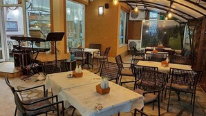 An outdoor dining area with tables and chairs, a music stand, and a view of the outdoors. - Complex Villa Brigantina (Nessebar)