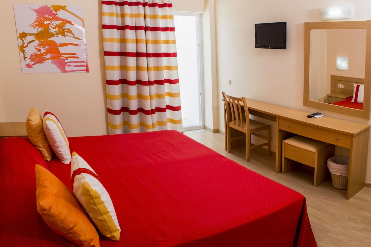 Una habitación de hotel con cama, escritorio, silla, televisión y espejo.