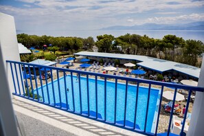 A pool area with lounge chairs and umbrellas, surrounded by trees and a view of the sea. - Hotel Delphi Beach - All Inclusive (Dorida)