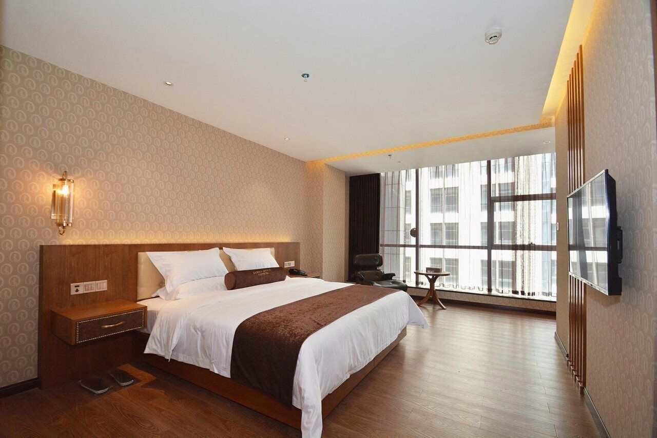 Hotelkamer met groot bed, nachtkastje, tv aan de muur en raam met uitzicht op gebouwen.
