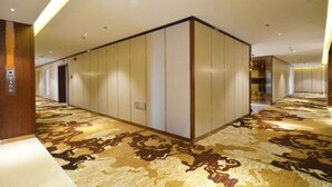 A hotel corridor with a patterned carpet, a wooden column, and a wall with vertical panels. - James Joyce Coffetel (Zhengzhou)
