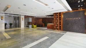 A modern interior with a reception desk labeled "James Joyce Coffee" and a seating area with a yellow chair. - James Joyce Coffetel (Zhengzhou)