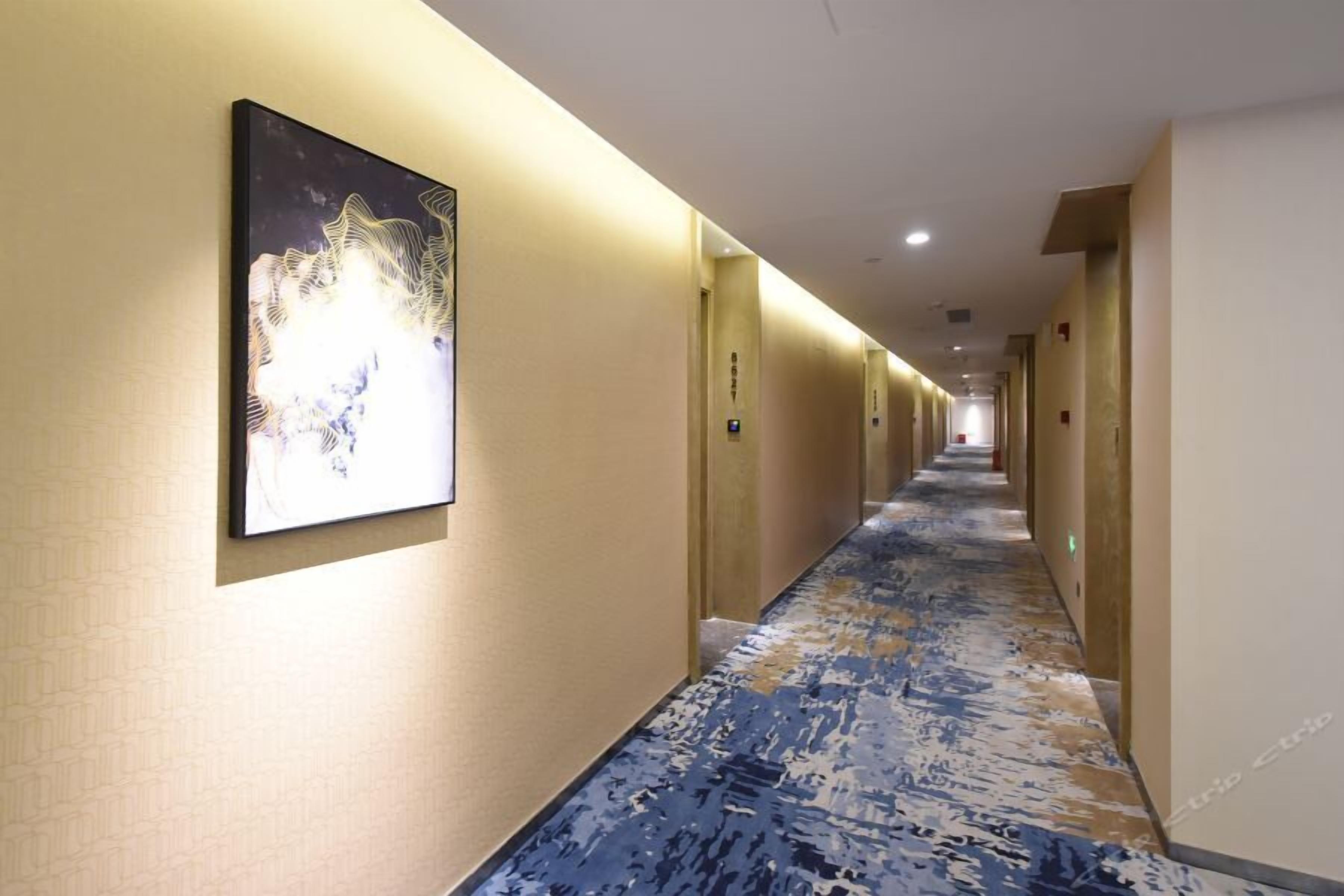 Un couloir d’hôtel avec un tapis à motifs, une œuvre d’art encadrée au mur et des portes de part et d’autre.