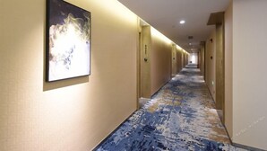 En hotellkorridor med ett mönstrat golv, ett inramat konstverk på väggen och dörrar på båda sidor.