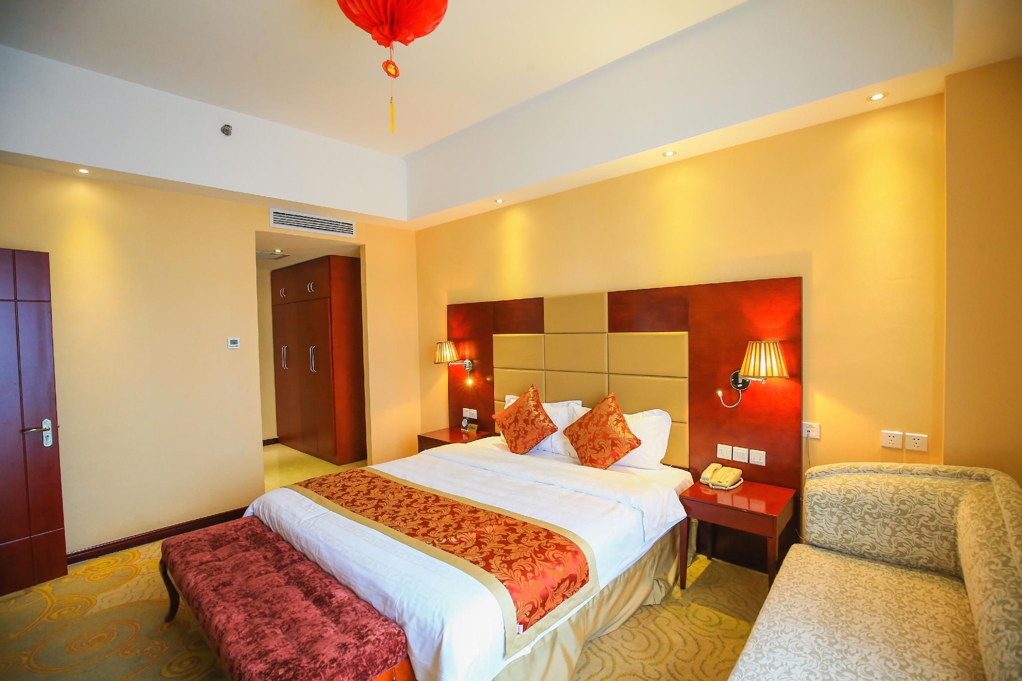 A hotel room with a large bed, bedside tables, a chair, and a red hanging decoration.
