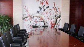 A conference room with a long table and multiple chairs, a large painting on the wall, and a potted plant.