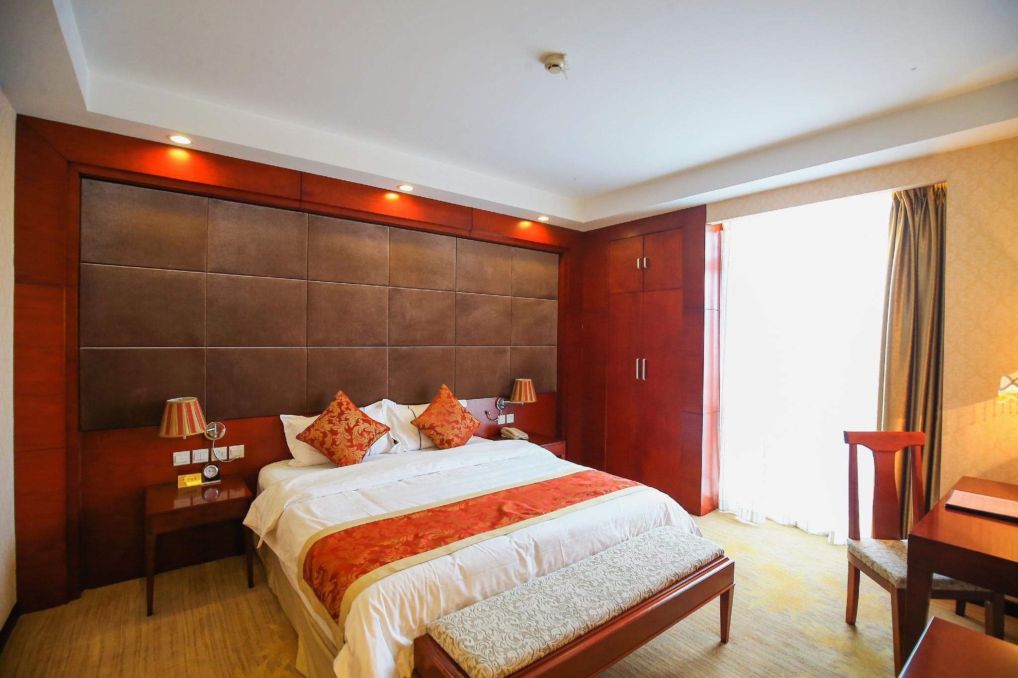 A hotel room with a large bed, wooden headboard, bedside tables, and a desk with a chair.