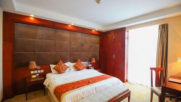 A hotel room with a large bed, wooden headboard, bedside tables, and a desk with a chair.