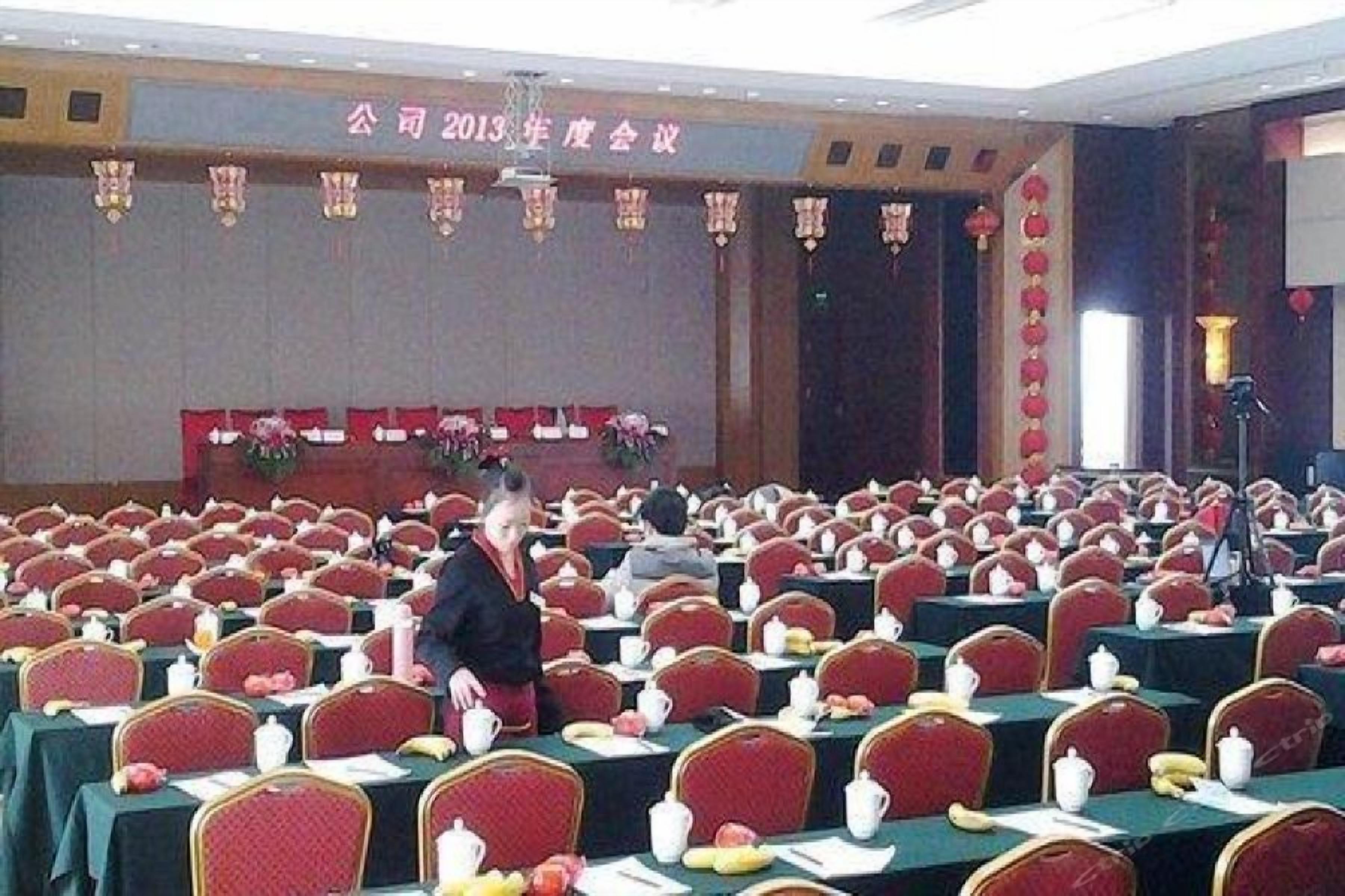 Un salón de conferencias con filas de mesas, sillas y un escenario con un cartel.