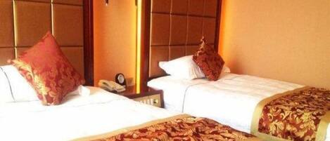 Une chambre d’hôtel avec deux lits, chacun recouvert d’une couvre-lit aux motifs rouges et dorés, doté d’une tête de lit et agrémenté d’une table de chevet avec une lampe.