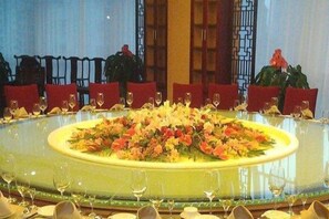 A round dining table with chairs, a central floral arrangement, and wine glasses. - Tianxinliang Hotel (Beijing)
