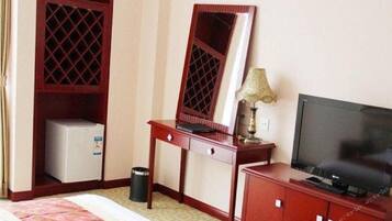 A hotel room with a bed, a desk with a computer, a television, a wardrobe, and a small refrigerator.