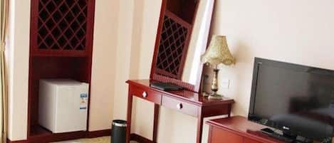 A hotel room with a bed, a desk with a computer, a television, a wardrobe, and a small refrigerator.